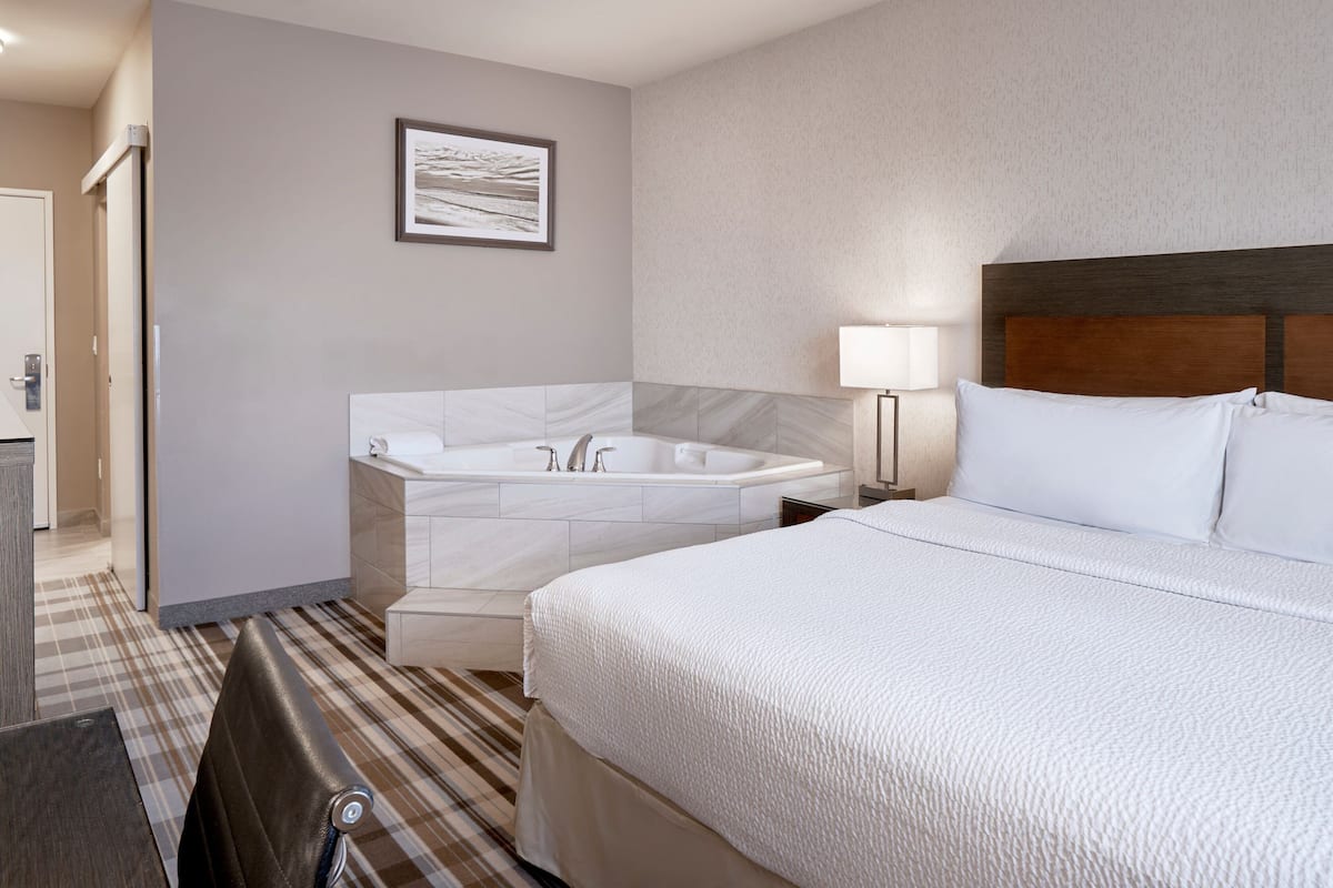 A hotel room with a large bed, a separate bathroom with a bathtub, a small seating area, and a framed picture on the wall.