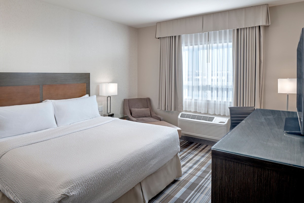 Une chambre d’hôtel avec un grand lit, un bureau, une chaise et une fenêtre avec des rideaux.