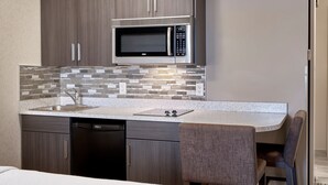 A compact kitchen with dark wood cabinets, a stainless steel microwave, a dishwasher, and a tiled backsplash. - Fairfield Inn & Suites by Marriott Airdrie (Airdrie)