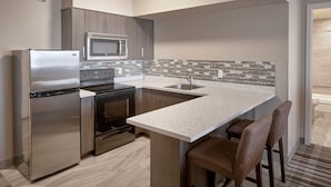 A modern kitchen with stainless steel appliances, a tiled backsplash, and a bar area with stools. - Fairfield Inn & Suites by Marriott Airdrie (Airdrie)