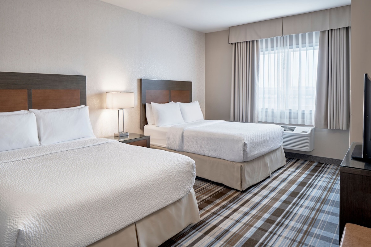 Habitación de hotel con dos camas, televisión, lámpara y ventana con cortinas.