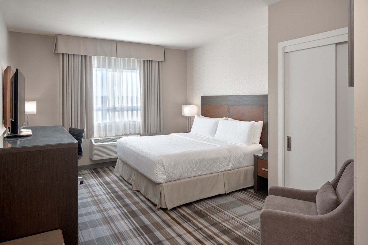 Une chambre d’hôtel avec un lit, un bureau, une chaise, une télévision et une fenêtre avec des rideaux.