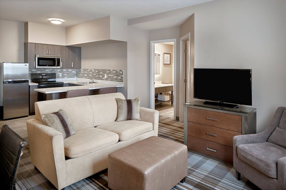 A modern living room with a sofa, ottoman, and a flat-screen TV.