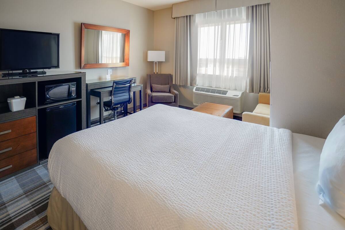 A hotel room with a large bed, a desk with a computer, a television, a microwave, and an air conditioning unit.