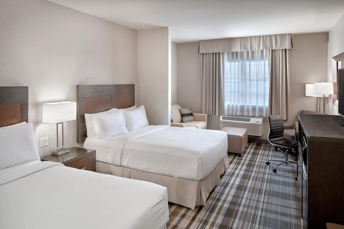 A hotel room with two beds, a desk, a chair, a lamp, and a large window with curtains.