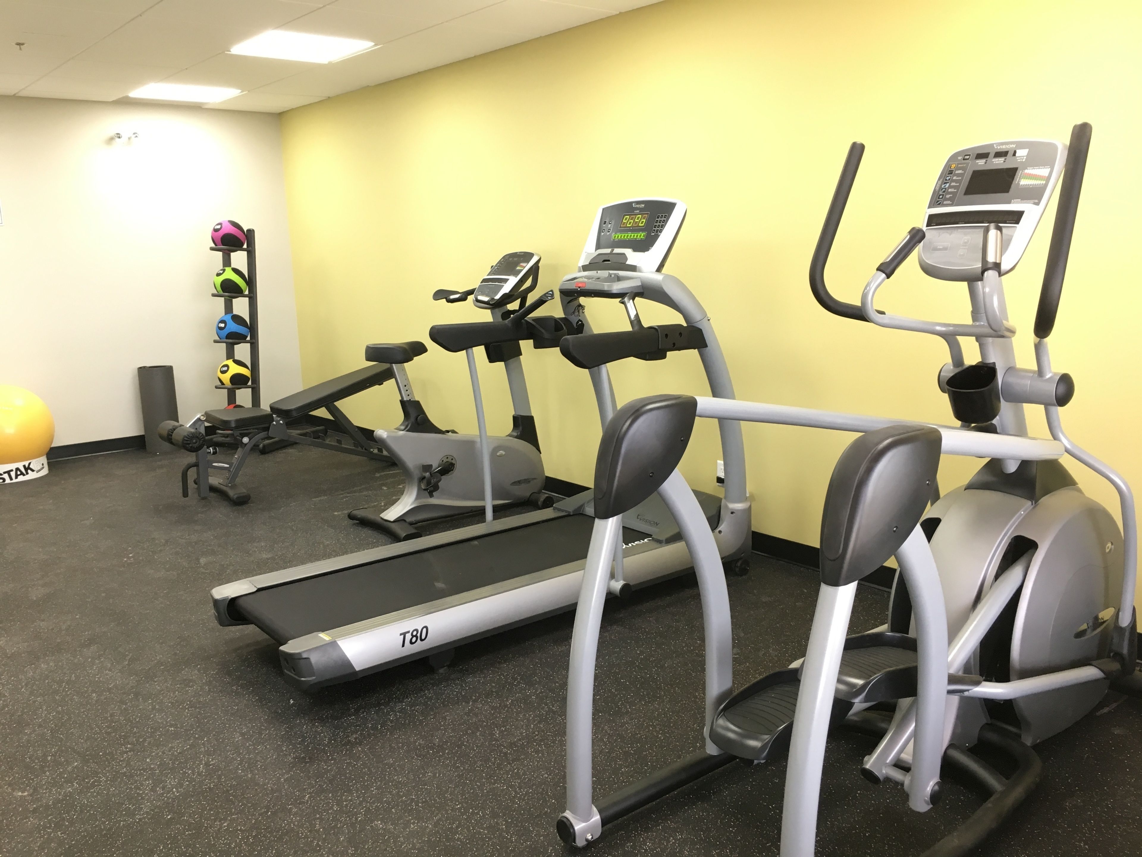 Un gimnasio con cintas de correr, elípticas y pelotas de ejercicio.