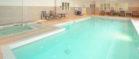 Una piscina interior con agua cristalina, bordes de azulejos y múltiples sillones de descanso alrededor.