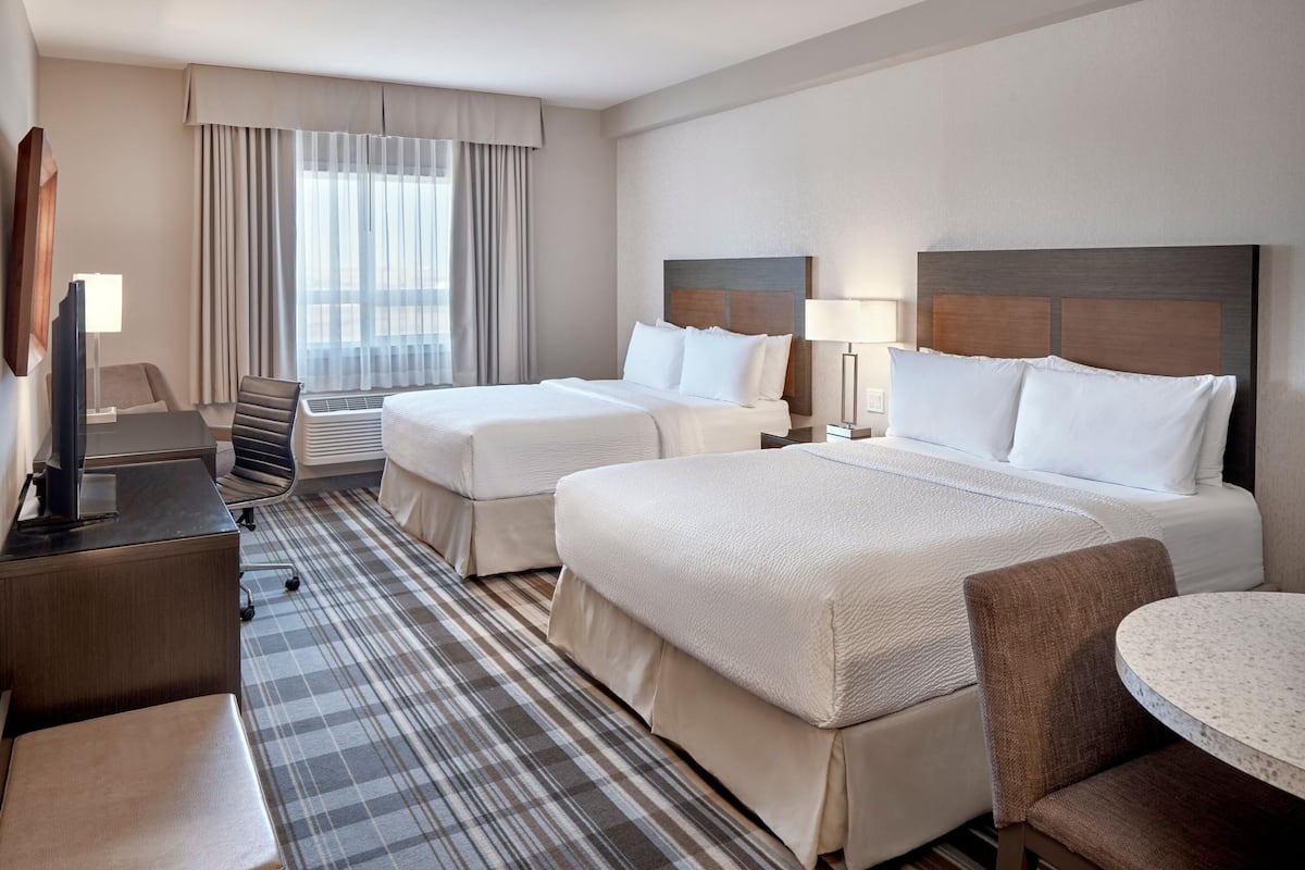A hotel room with two beds, a desk, a chair, a TV, and a window with curtains.