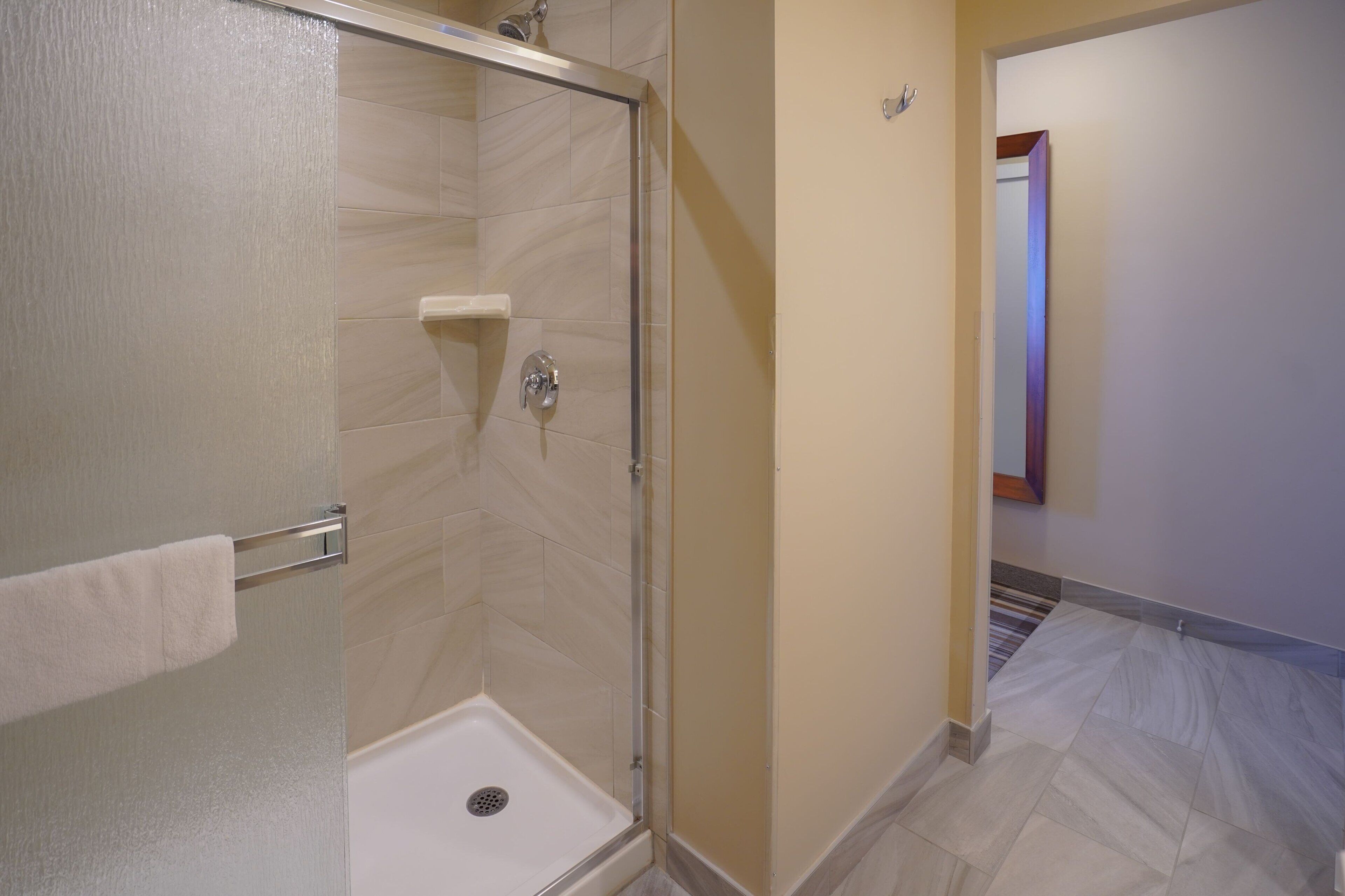 A bathroom with a glass-enclosed shower, a towel rack, and a tiled floor.