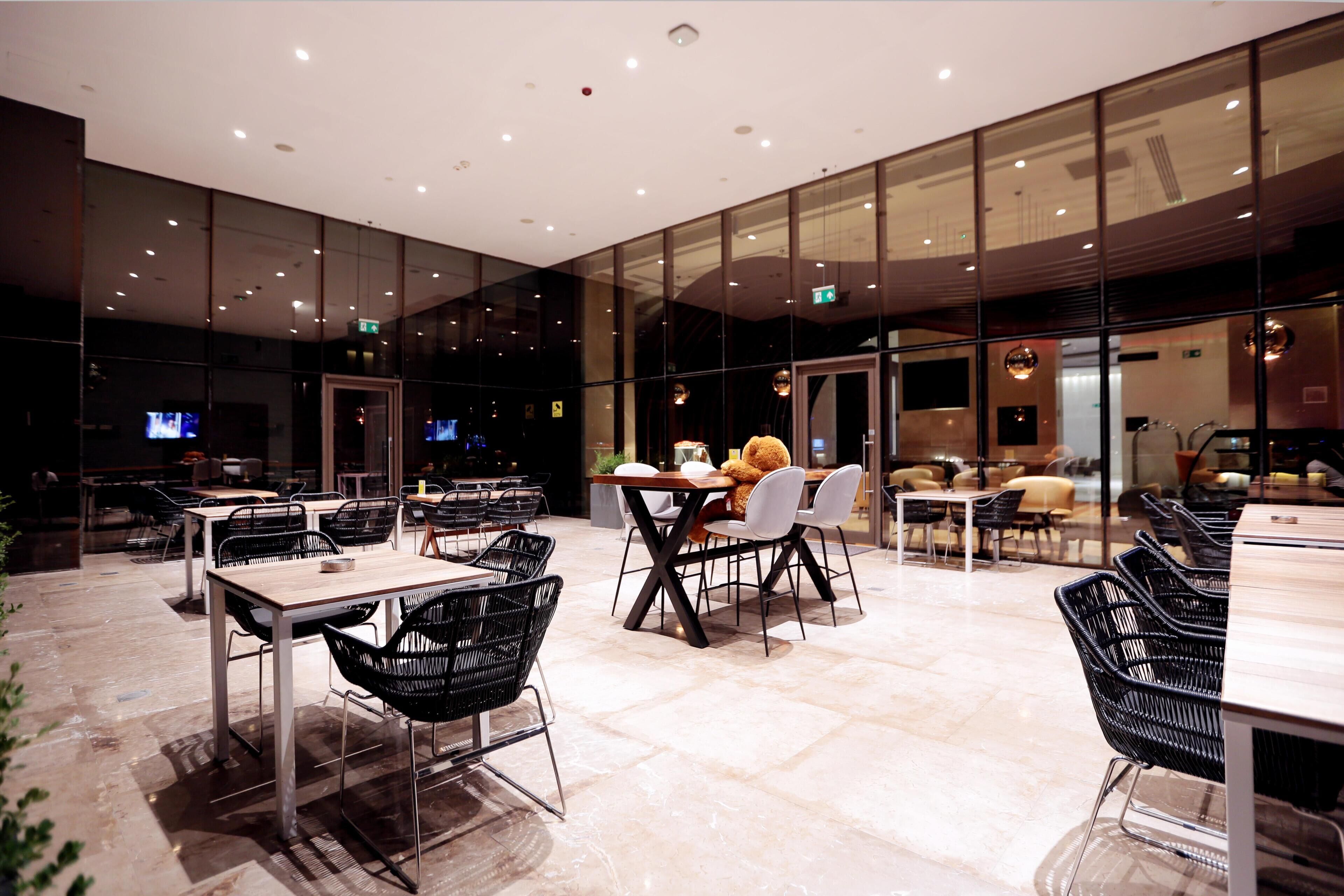 A modern restaurant with glass walls, multiple tables, and black chairs.