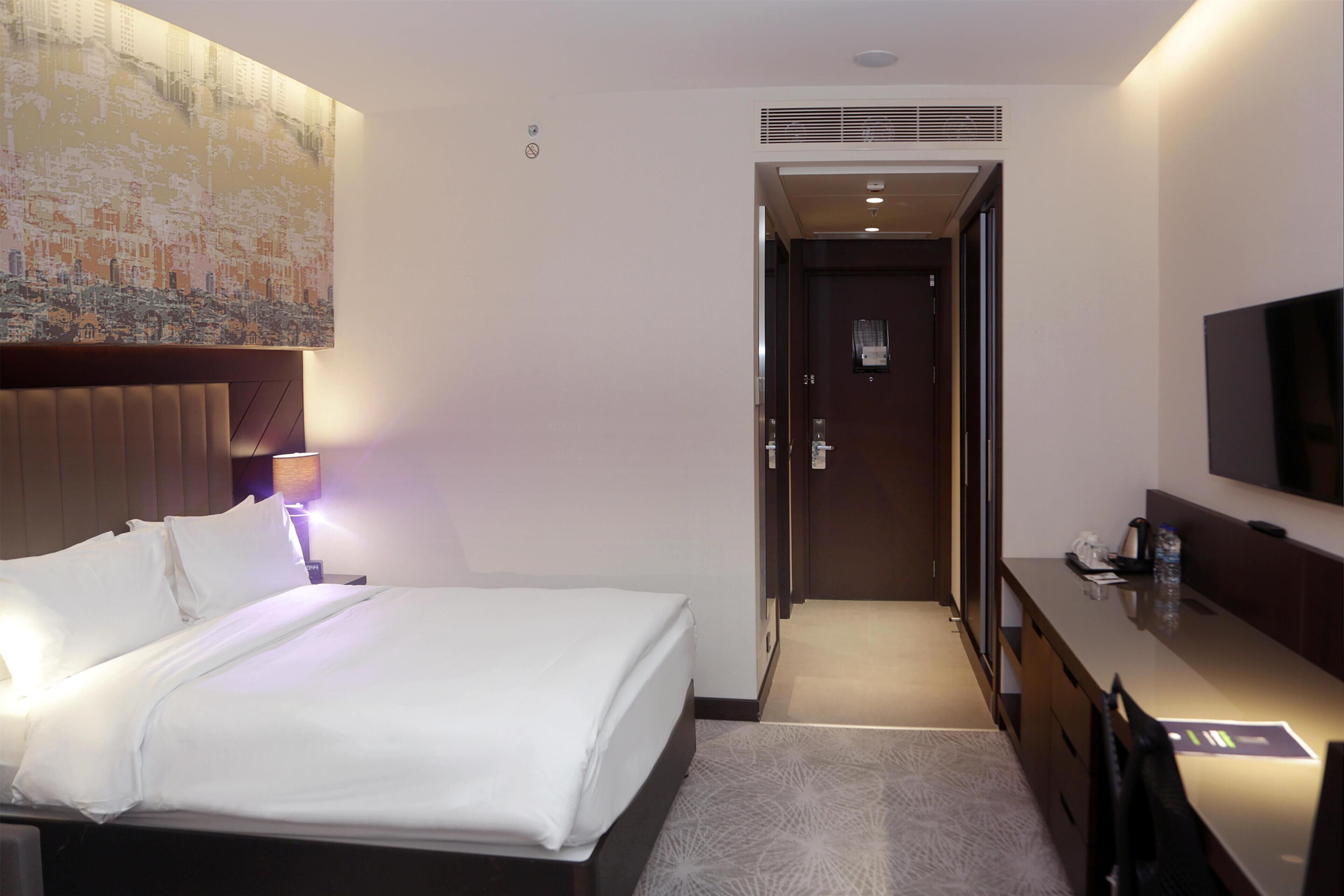 Une chambre d’hôtel équipée d’un lit, d’un bureau, d’une télévision et d’une porte donnant sur une autre pièce.
