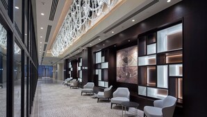 Eine moderne Hotellobby mit einer langen Korridor, einer Sitzgelegenheit mit Stühlen und Tischen sowie einer dekorativen Deckenleuchte.