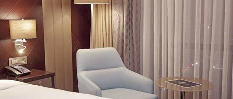 Une chambre d’hôtel avec un lit, une chaise, une petite table, une lampe et un téléphone sur une table de chevet.