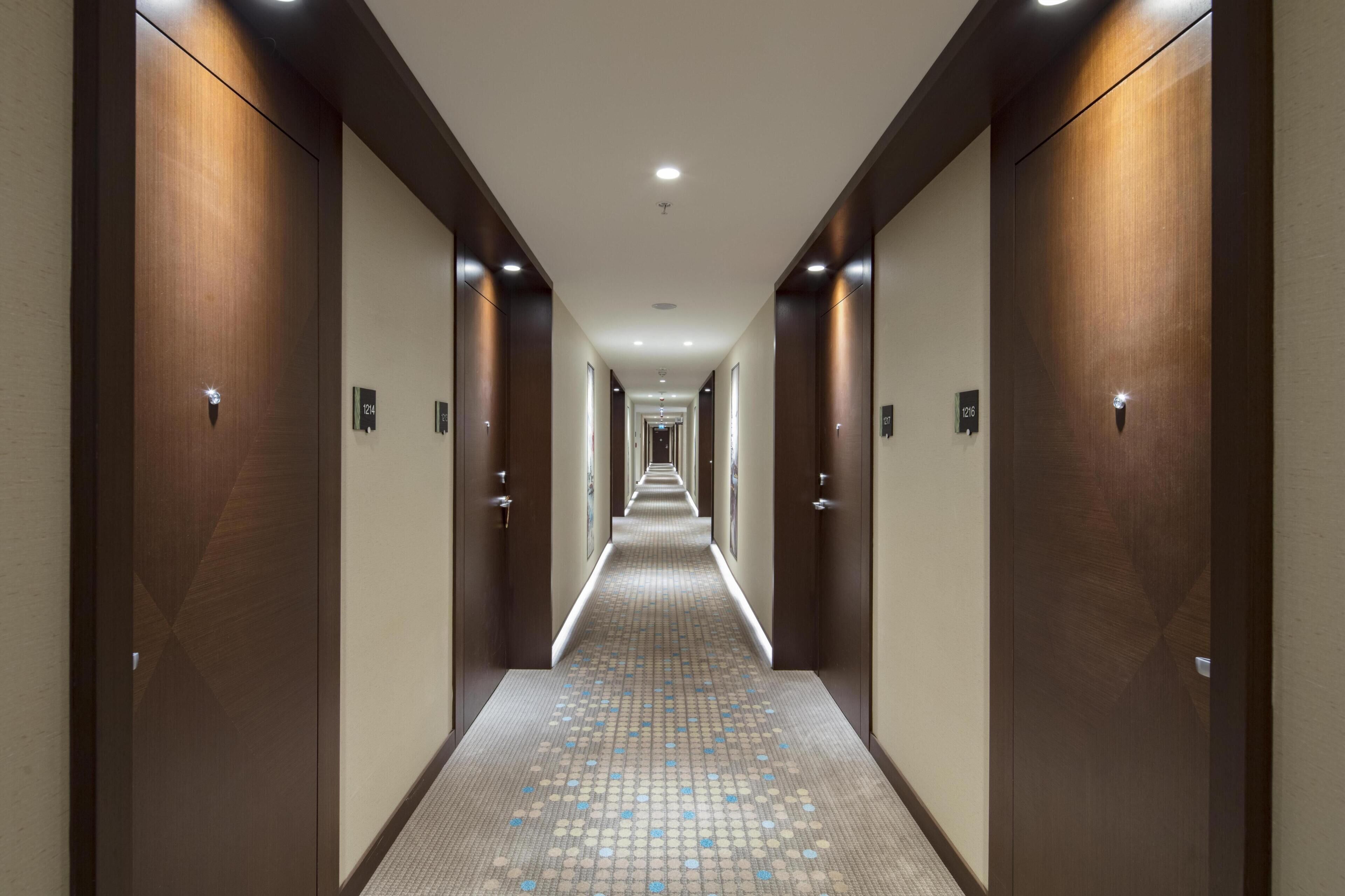A hotel hallway with wooden doors, numbered room signs, and a patterned floor.