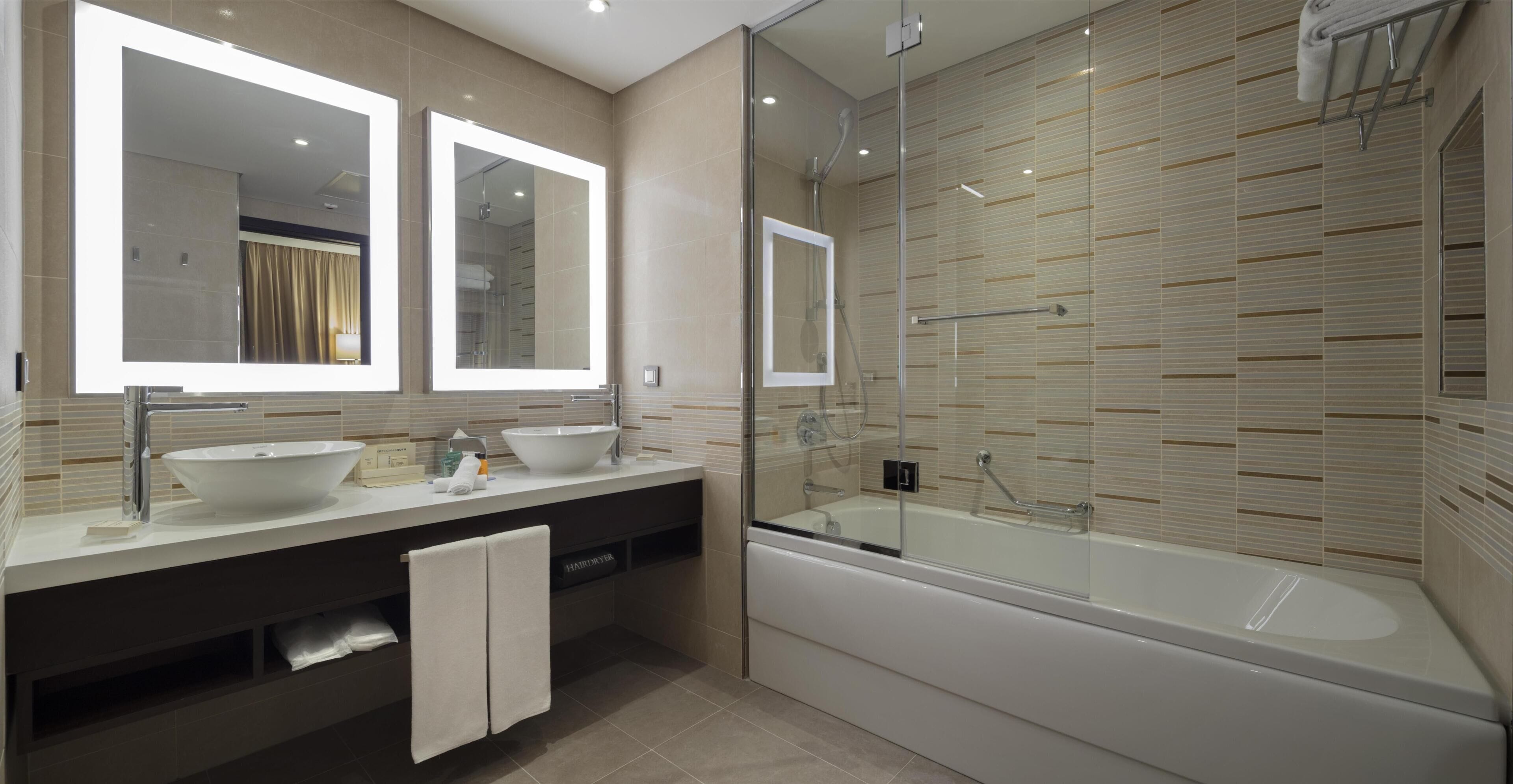 Une salle de bain moderne avec deux lavabos, un grand miroir et une douche séparée par une paroi de verre.