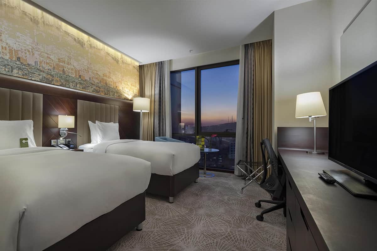 A hotel room with two beds, a television, and a cityscape view.