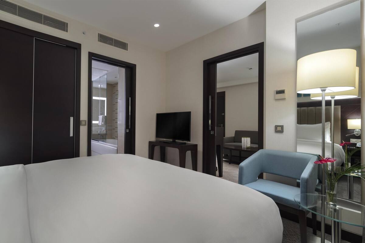 A hotel room with a large bed, a TV, a seating area, and a mirror.