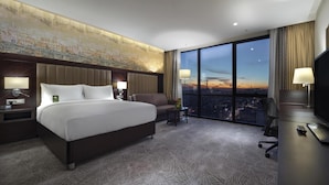 Ein Hotelzimmer mit einem großen Bett, einem Schreibtisch, einem Fernseher und Blick auf die Stadt.