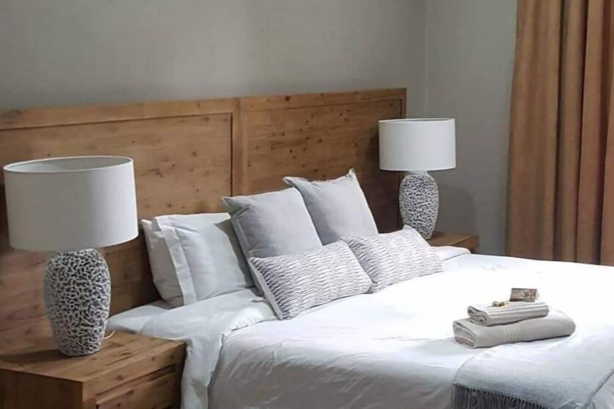 A neatly made bed with white linens and multiple pillows, flanked by wooden nightstands with lamps.