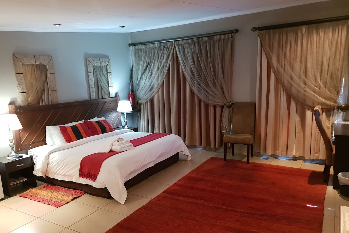 A hotel room with a large bed, a nightstand with a lamp, a chair, and a red rug.