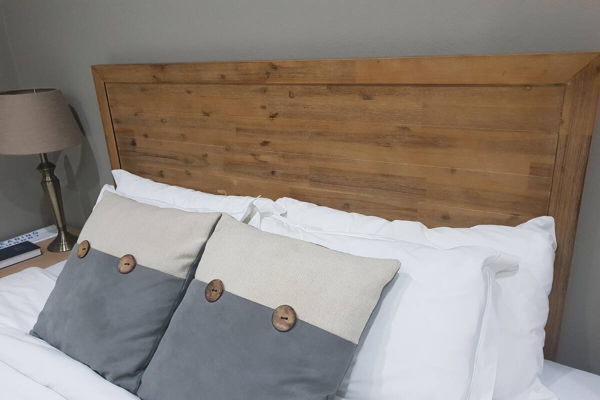 A bed with a wooden headboard, two grey pillows with wooden buttons, and white bedding.