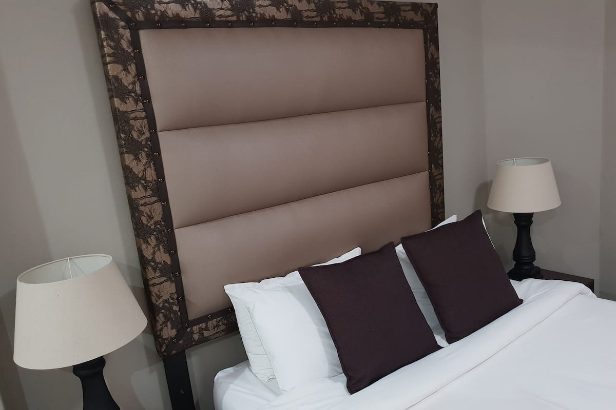 A neatly made bed with a headboard, two bedside lamps, and two pillows.
