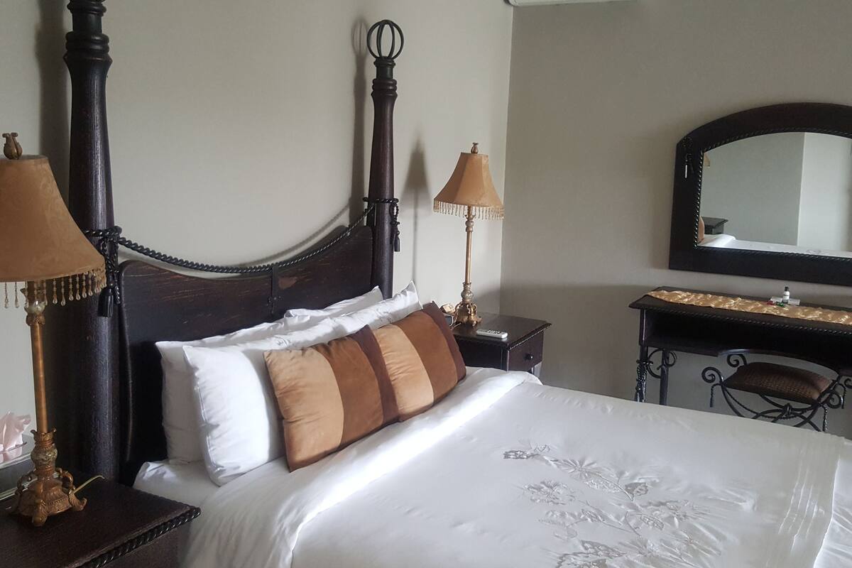 A hotel room with a large bed, two bedside lamps, a mirror, and a dresser.