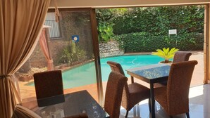 Une pièce dotée d’une porte vitrée donnant sur une piscine, d’une table avec des chaises et offrant une vue sur la verdure environnante.