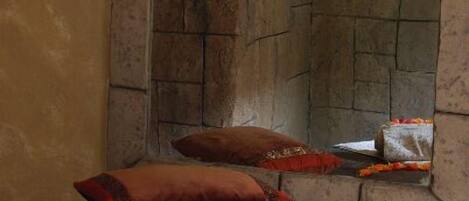 A room with a stone fireplace, a candle on a wall-mounted holder, a bed with a dark cover, and a towel with flowers.