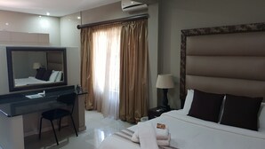 Une chambre d’hôtel équipée d’un lit, d’un bureau, d’une chaise, d’un miroir, d’une lampe et d’une fenêtre avec des rideaux.