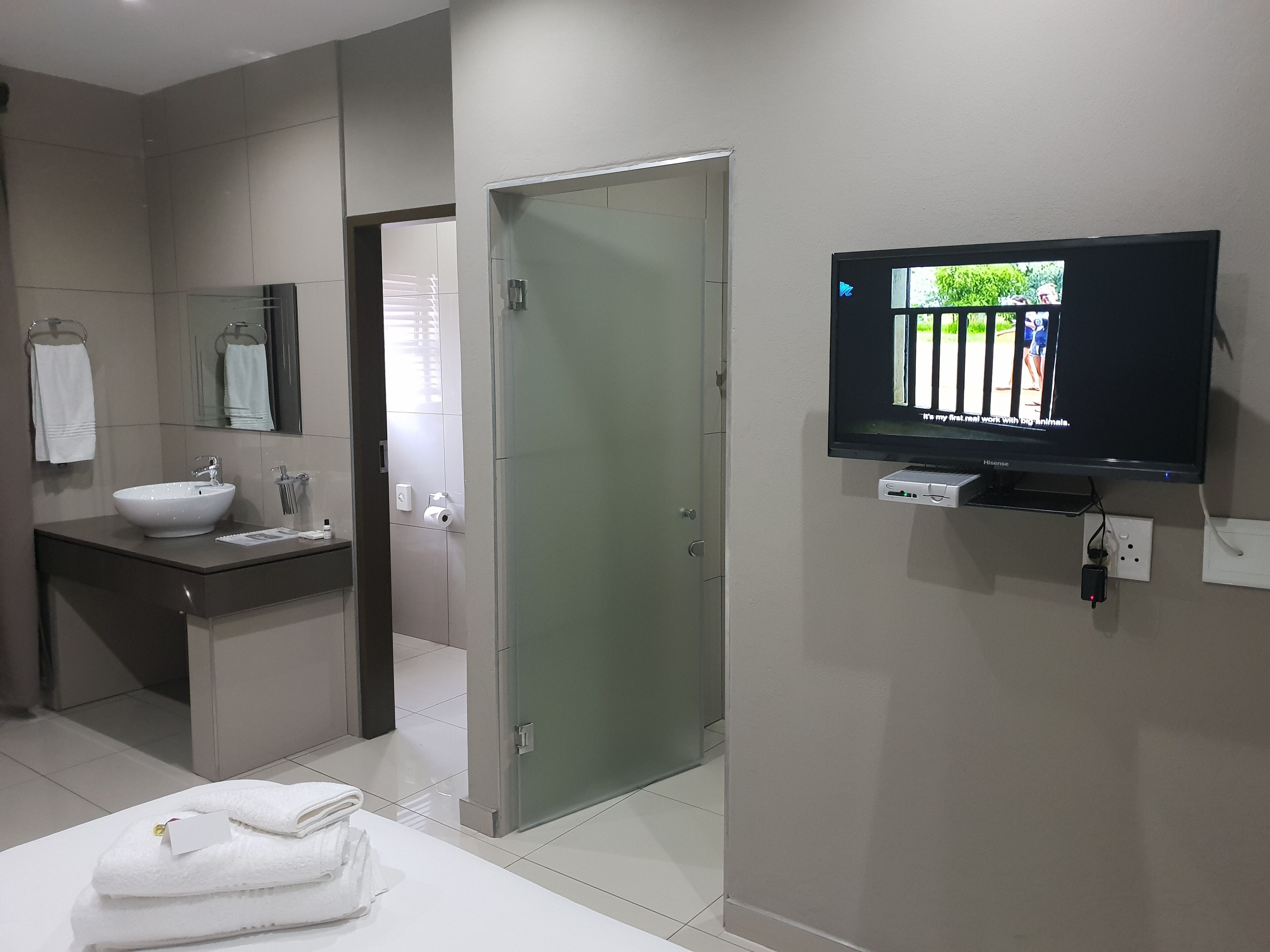 A modern bathroom with a large mirror, a sink, a toilet, and a television mounted on the wall.