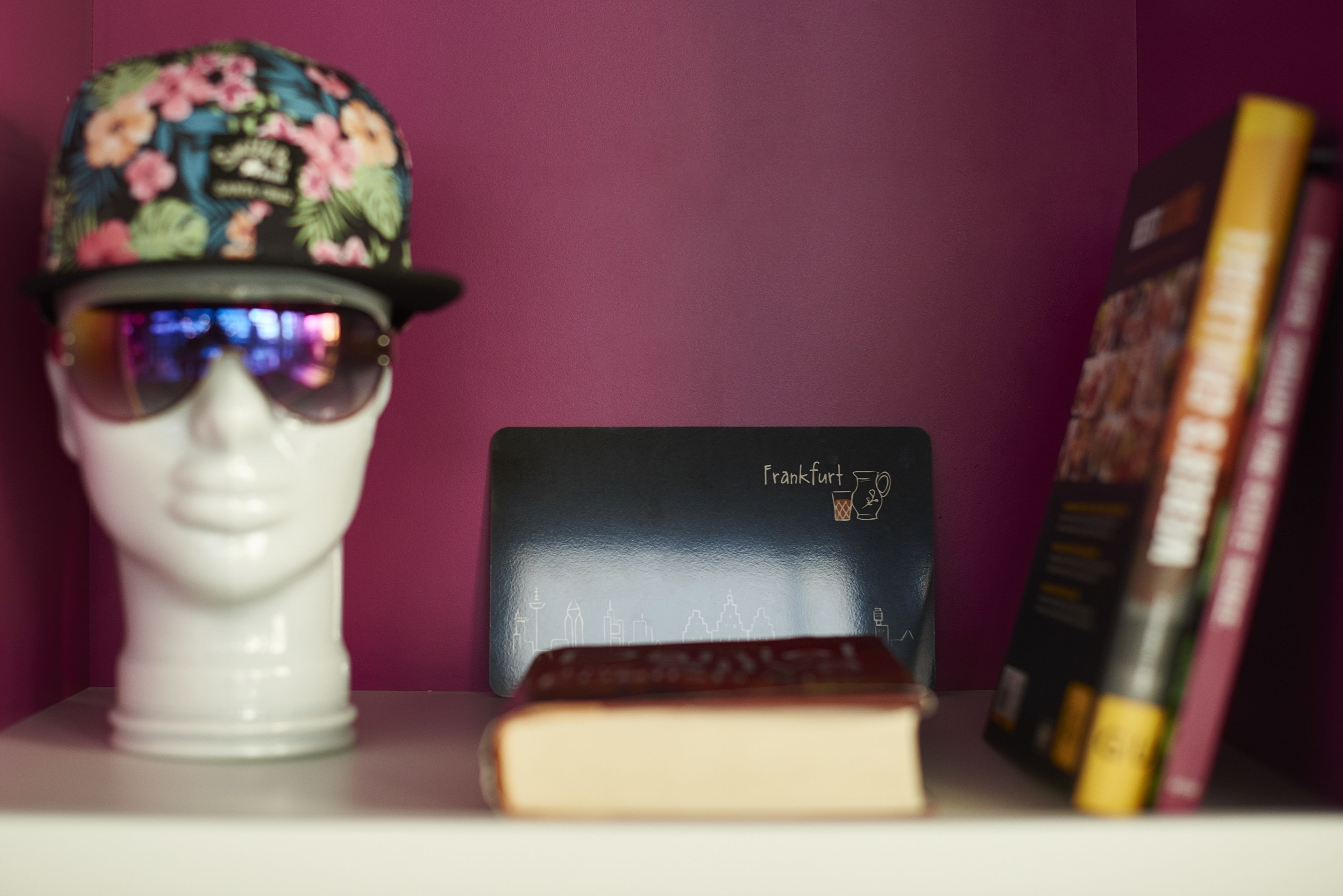 A mannequin head with a floral hat, a book, and a black wallet with a city skyline on it.
