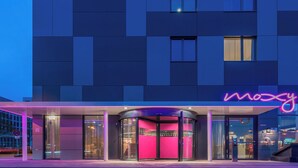 Une entrée d’hôtel moderne avec une porte tournante en verre, un panneau lumineux au néon et une vue dégagée sur l’intérieur à travers le verre.