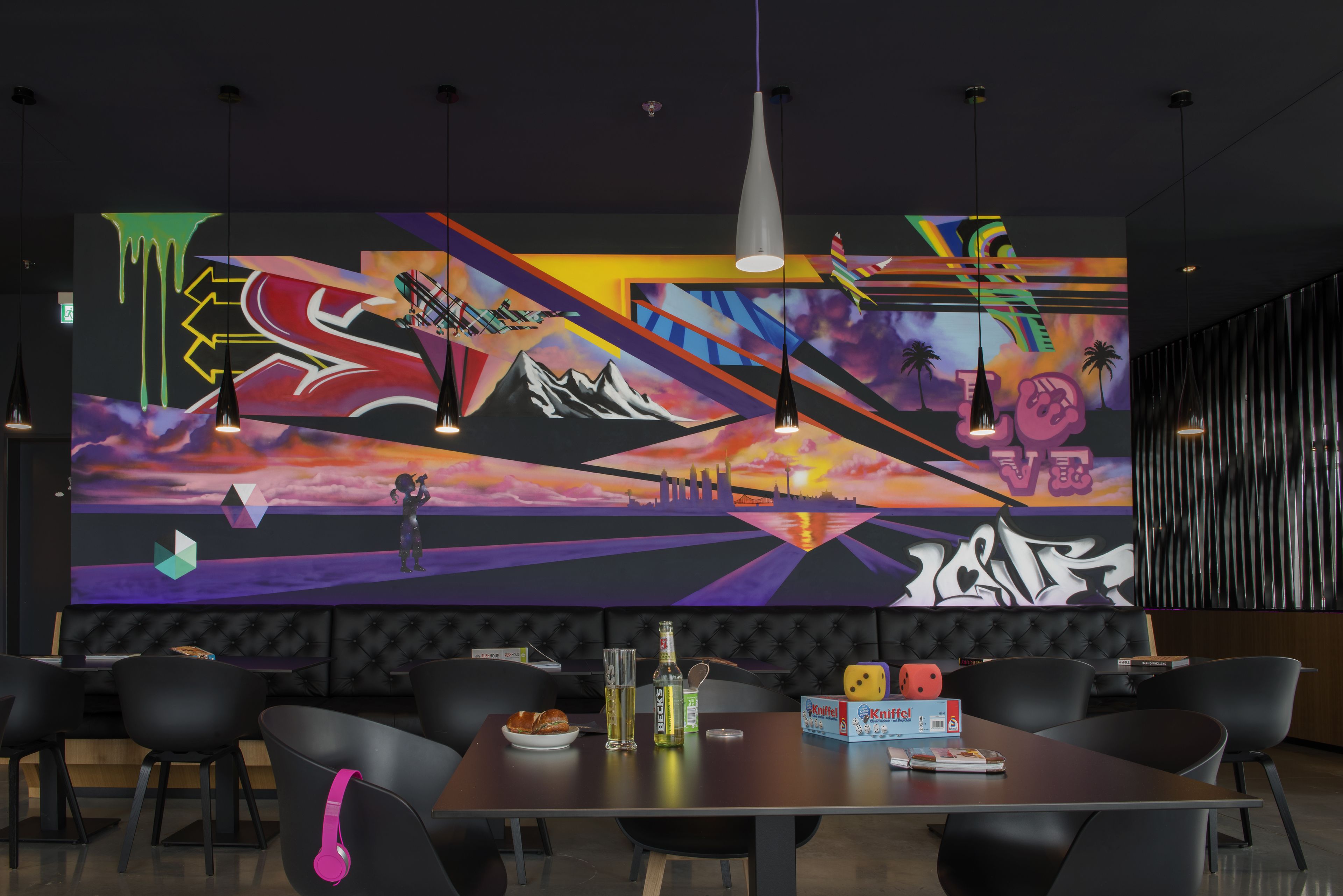 Un comedor moderno con un gran mural, sillas tapizadas en negro, una mesa de madera e iluminación colgante.