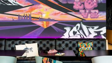 Ein moderner Lounge-Bereich mit einem schwarzen, gepolsterten Sofa, bunten Kissen und einem großen, abstrakten Wandgemälde.