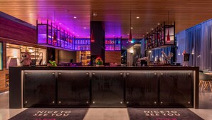 Un espace d’accueil d’hôtel au design moderne, comprenant un bar avec un assortiment de bouteilles, un jouet en peluche et un panneau sur lequel on peut lire : « Ravi de vous revoir. »