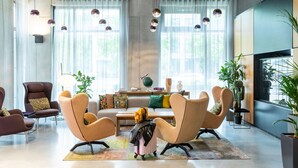 Un salon moderne comprenant un canapé, deux fauteuils, une table basse et une lampe. De grandes fenêtres sont ornées de rideaux légers et de luminaires sphériques suspendus.