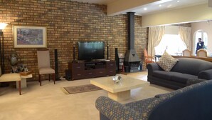 A living room with a brick wall, a fireplace, a television, and a sofa. - Ah Ha Guest House (Germiston)