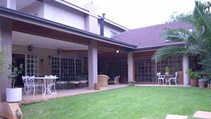 A covered patio with outdoor seating, a lawn, and a tiled roof. - Ah Ha Guest House (Germiston)