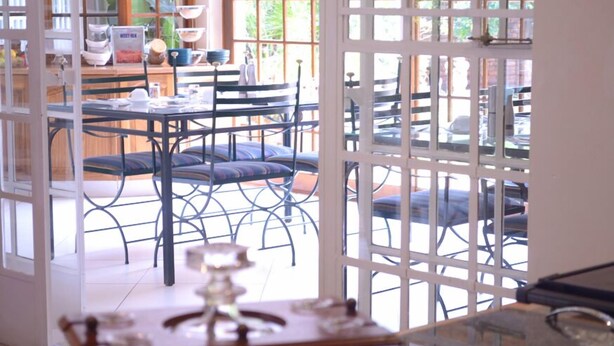 A dining area with a glass partition, metal chairs, and a table set for dining. - Ah Ha Guest House (Germiston)