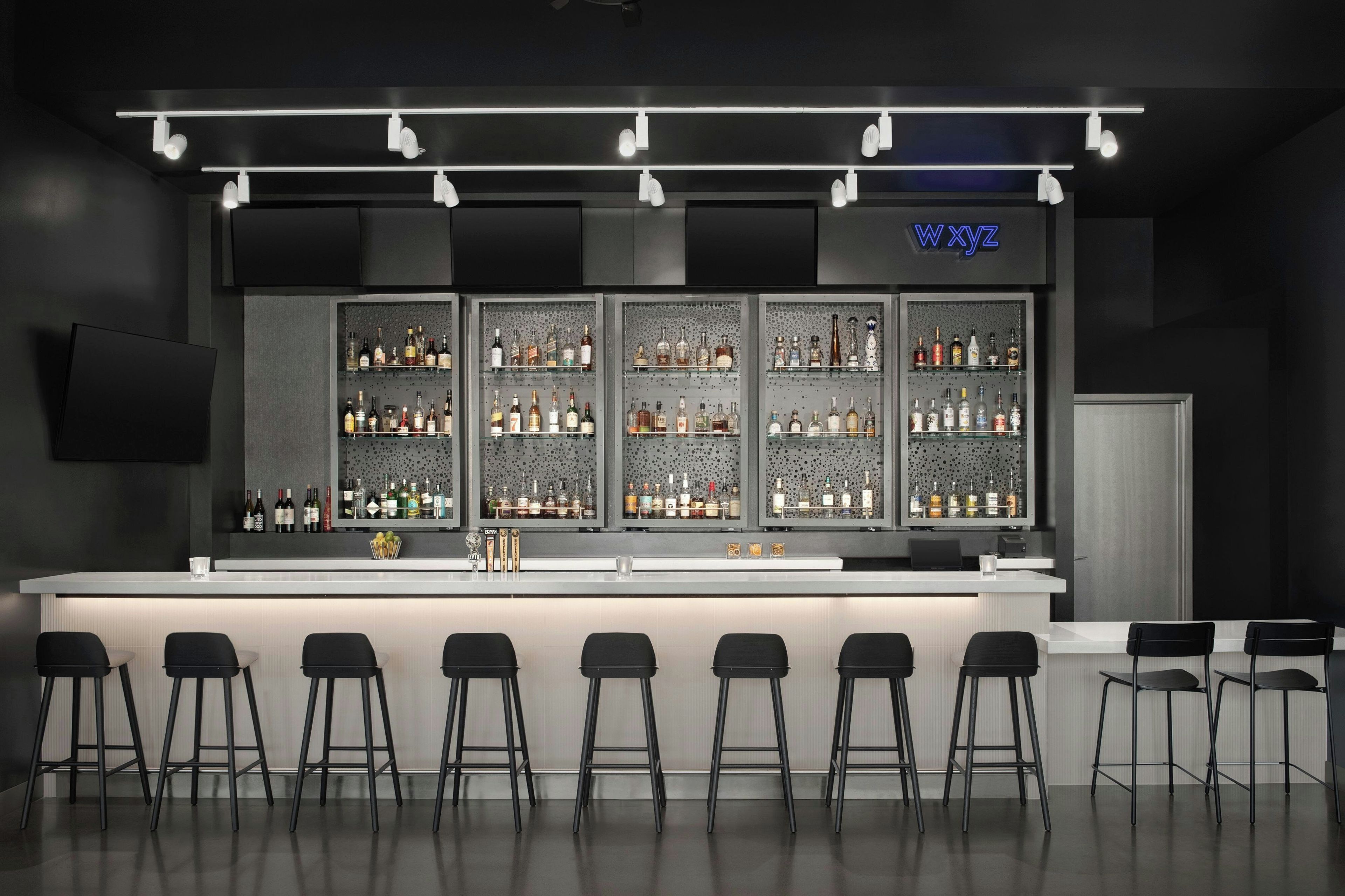 A bar area with a long counter, multiple shelves of bottles, and several black bar stools.