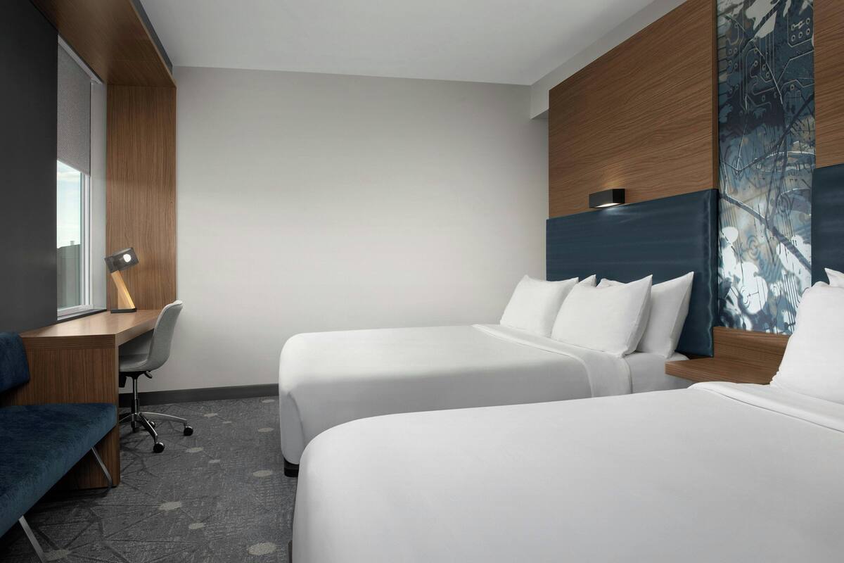 A hotel room with two beds, a desk, and a chair.