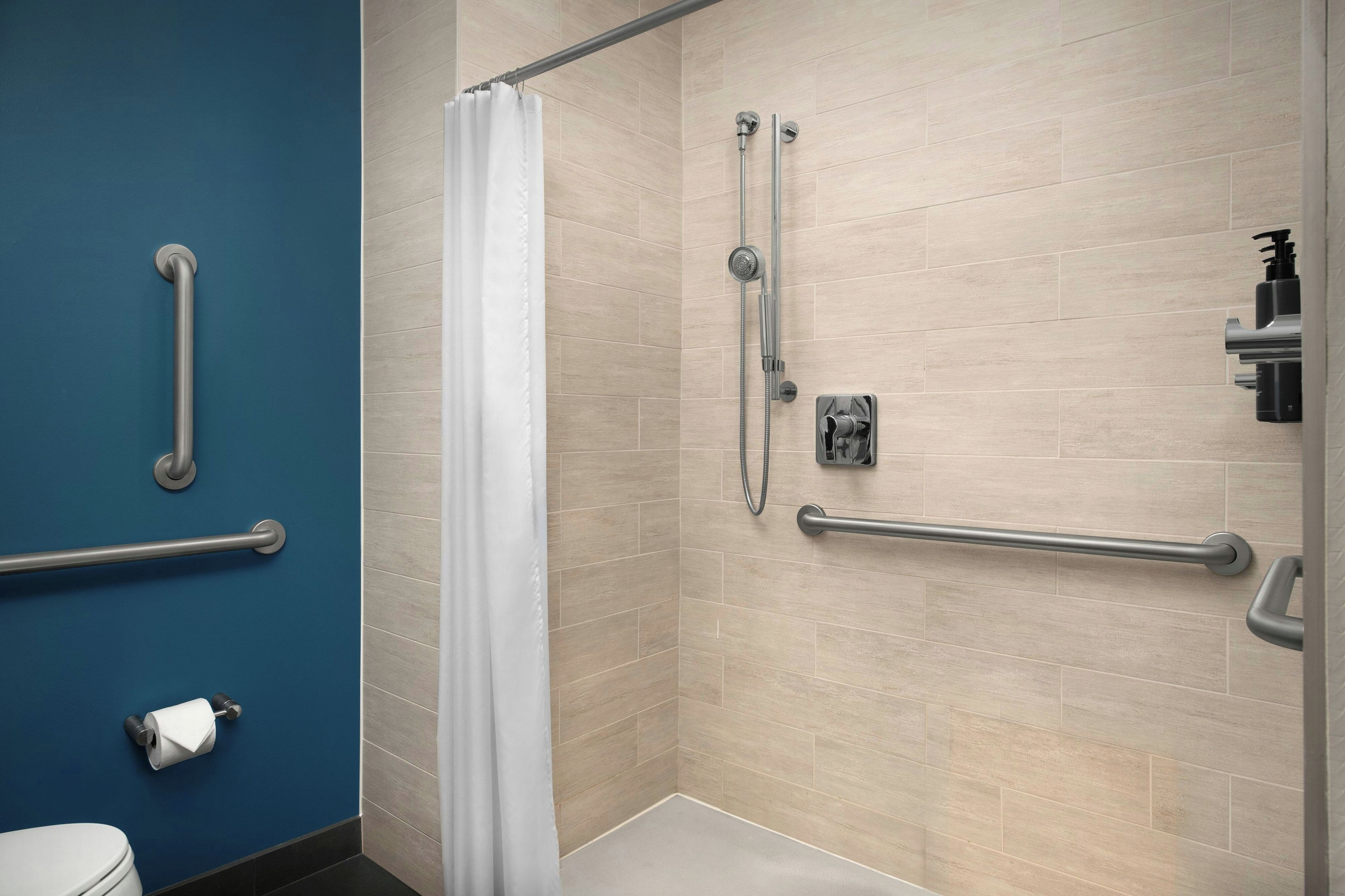 A bathroom with a shower, grab bars, and a toilet.