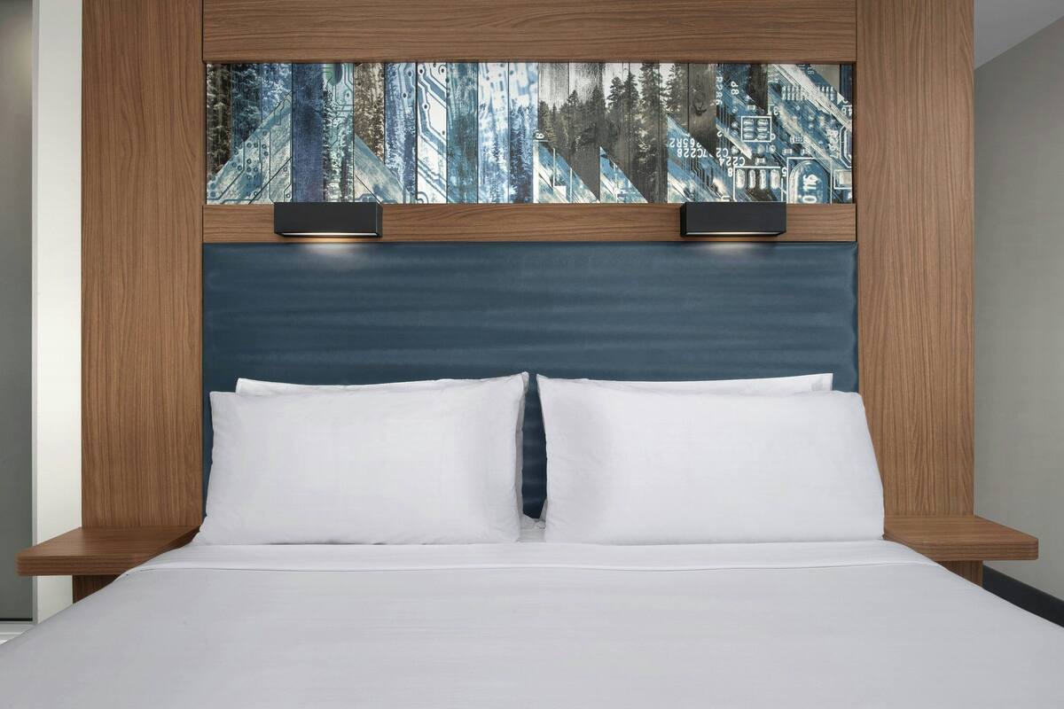 A bed with a headboard featuring a cityscape artwork, two bedside lamps, and a wooden frame.