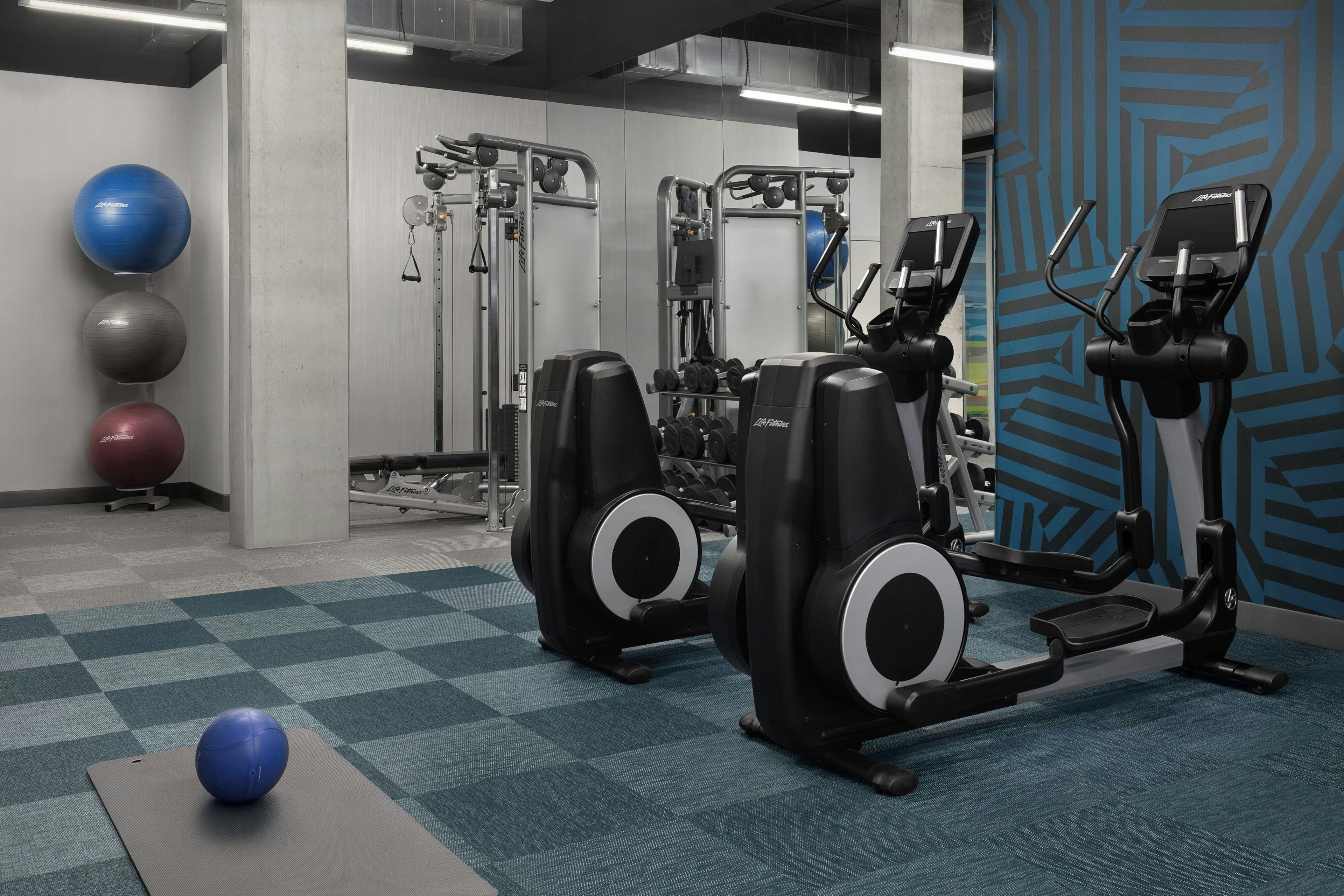 Ein Fitnessraum mit Trainingsgeräten, einer blauen Wand mit Muster und Übungsbällen.