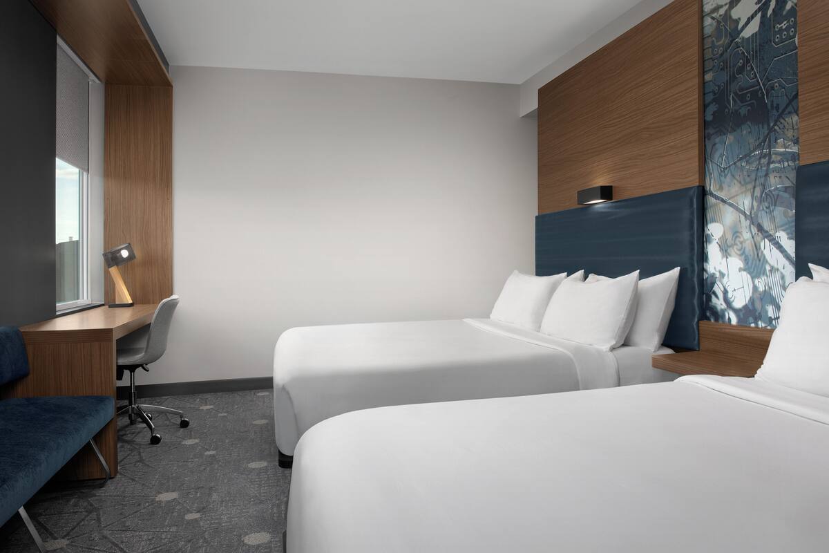 A hotel room with two beds, a desk, a chair, and a large abstract painting on the wall.