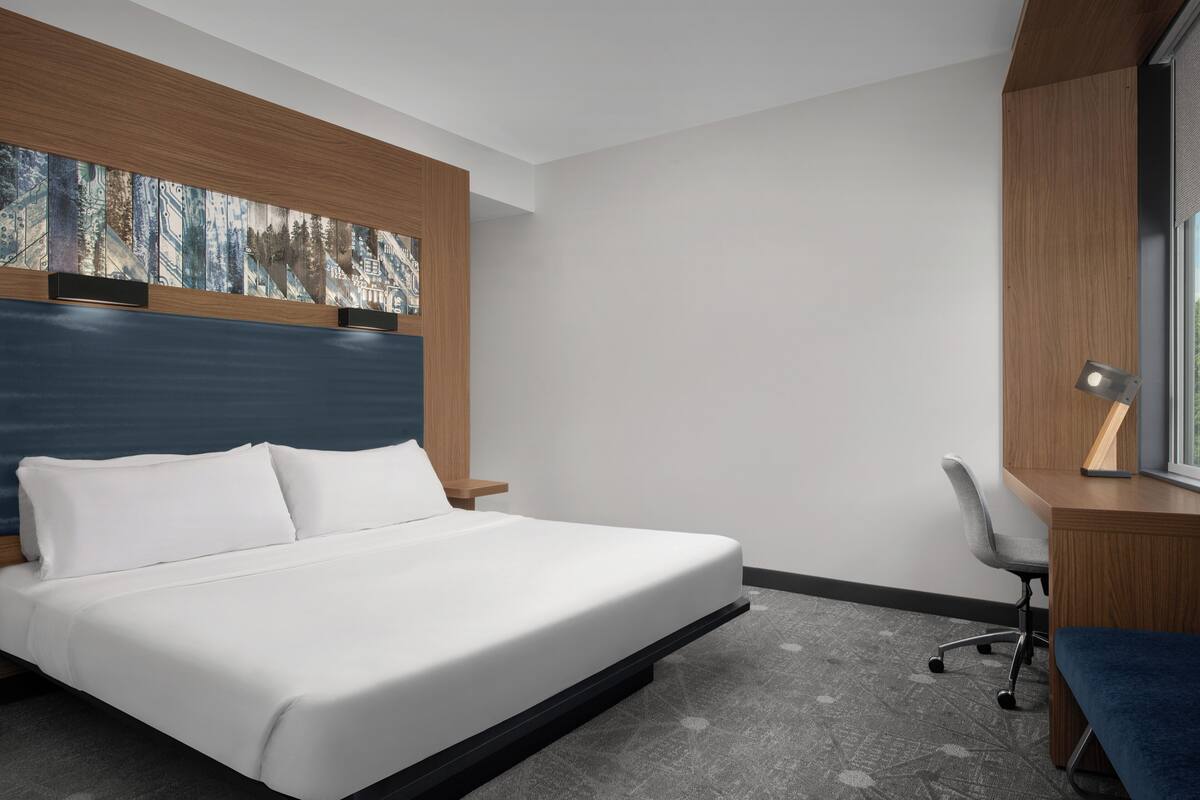 A modern hotel room with a large bed, a desk, and a chair.