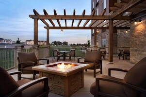 Un patio al aire libre con un hogar para fuego, pérgola de madera y zona de estar.