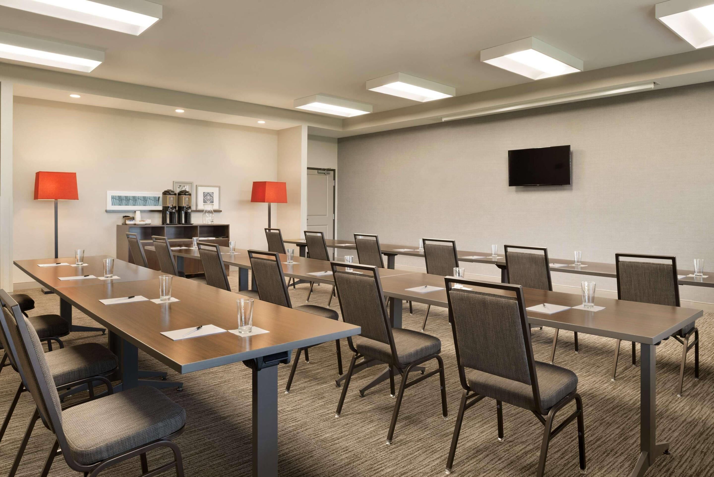Un salón de conferencias con mesas, sillas y una televisión en la pared.