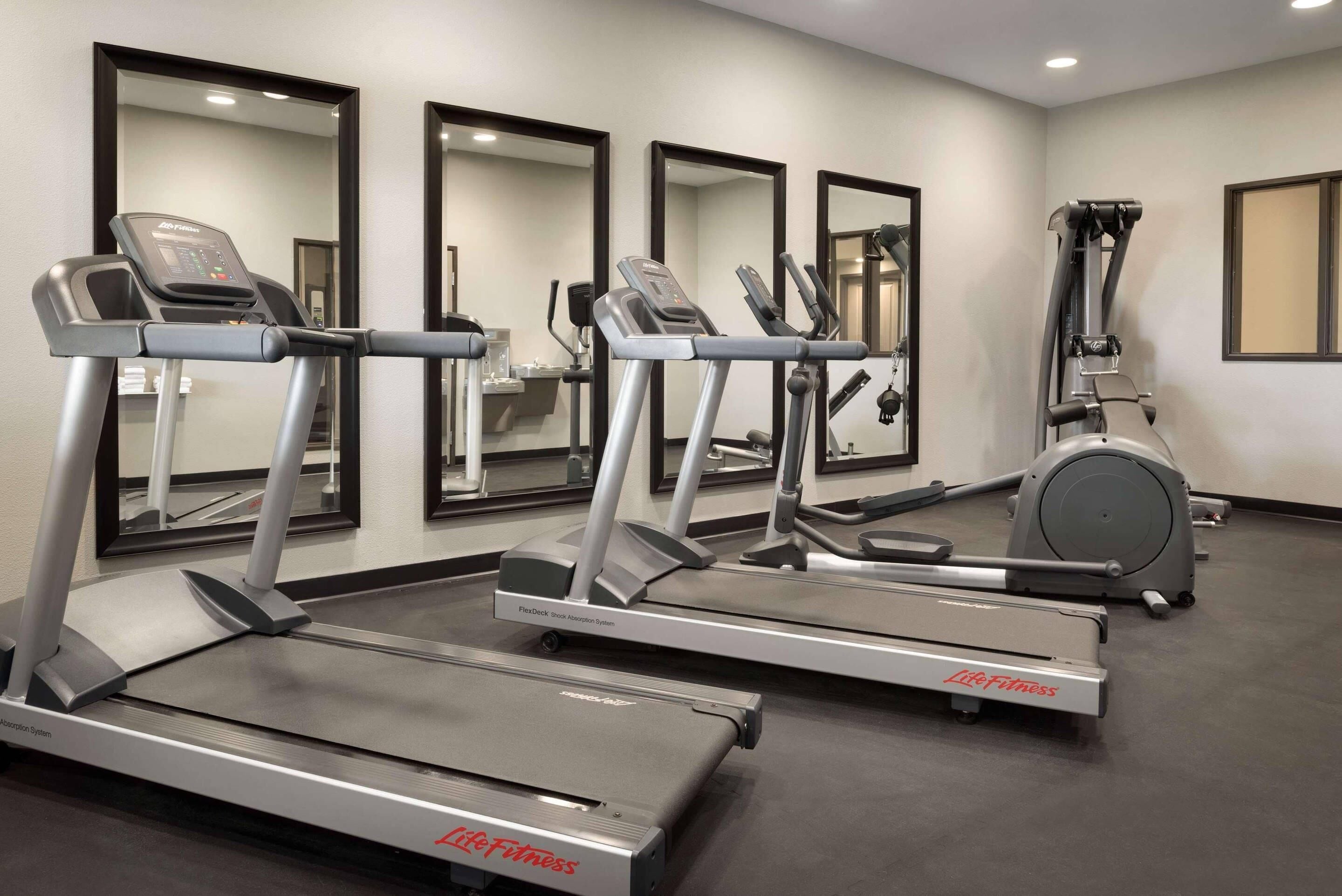 A gym with treadmills, ellipticals, and a stationary bike, with mirrors on the walls and a clean, modern design.